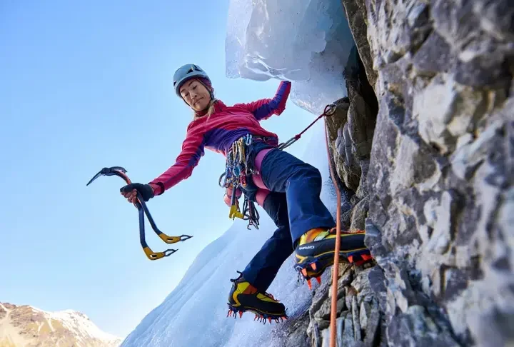 Skilled mixed climber transitioning from ice to rock, using ice tools and crampons on both surfaces, illustrating a guide to mastering mixed climbing essentials.