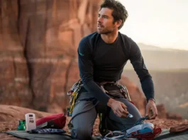 An experienced climber organizing next-level safety gear, including a PLB and first-aid kit, at the base of a cliff, illustrating essential climb safety beyond the basics.
