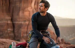 Next-Level Climb Safety: More Essential Gear Now An experienced climber organizing next-level safety gear, including a PLB and first-aid kit, at the base of a cliff, illustrating essential climb safety beyond the basics.