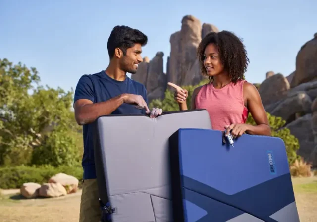 Two diverse climbers outdoors choosing from various bouldering crash pads, illustrating a full guide on how to choose the right crash pad.