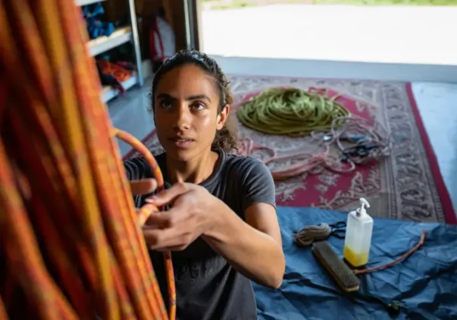 A climber embodying rope safety by inspecting a rope, with care items nearby and a retired rope repurposed as a mat, covering the full inspect, care, and retire guide.