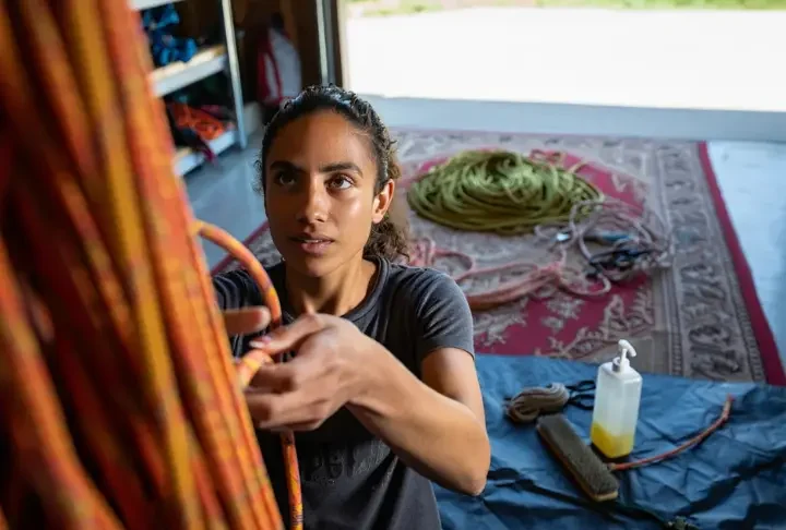 A climber embodying rope safety by inspecting a rope, with care items nearby and a retired rope repurposed as a mat, covering the full inspect, care, and retire guide.