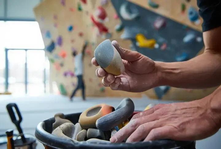 Close-up of route setter's hands selecting a climbing hold, symbolizing the secret of how gym climb grades emerge through route setting.