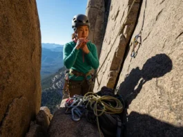 A female climber at a belay station on a multi-pitch route, assessing her gear to perform a simple partner rescue for a stuck or injured climber.