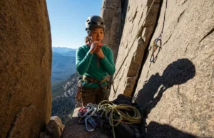 Simple Partner Rescue: For Stuck or Injured Climbers A female climber at a belay station on a multi-pitch route, assessing her gear to perform a simple partner rescue for a stuck or injured climber.