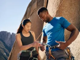 Two diverse climbers performing a pre-climb partner check at the base of a cliff, illustrating a key aspect of life-saving prevention from common climbing dangers.