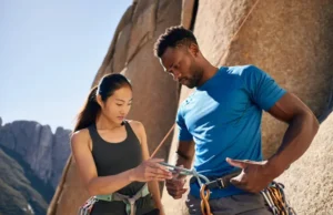 Top 10 Climbing Dangers & Life-Saving Prevention Two diverse climbers performing a pre-climb partner check at the base of a cliff, illustrating a key aspect of life-saving prevention from common climbing dangers.