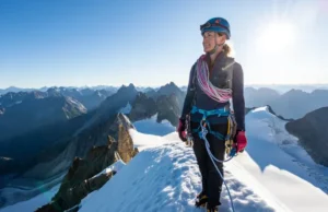 Unlock Alpine Success: Fundamental Skills Guide Alpinist on a snowy summit with ice axe and rope, overlooking mountain vista, having unlocked alpine success through fundamental climbing skills.