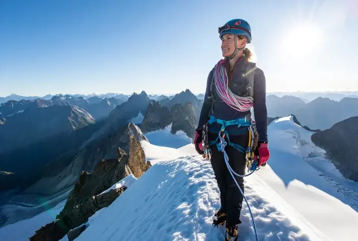 Alpinist on a snowy summit with ice axe and rope, overlooking mountain vista, having unlocked alpine success through fundamental climbing skills.