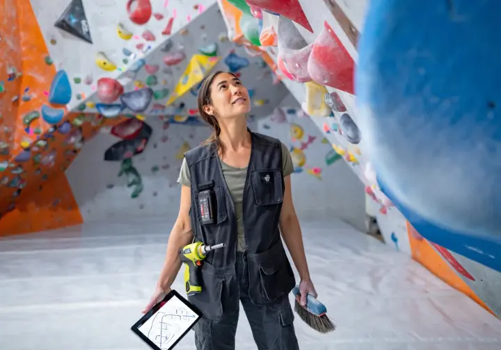 Profile of a modern female route setter thoughtfully examining a new bouldering route in a climbing gym, illustrating the architects of ascent.