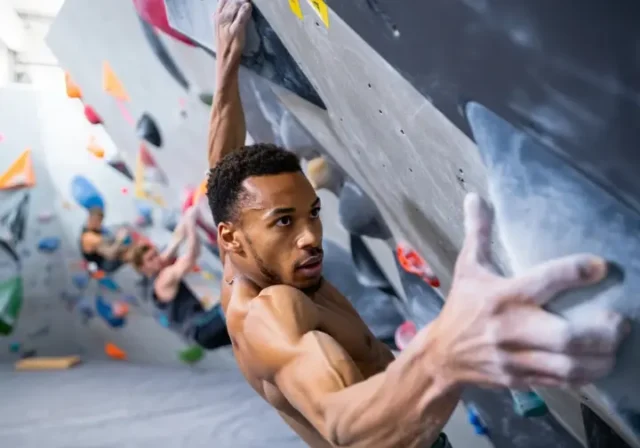 Boulderer executing a powerful move on an indoor wall, showcasing bouldering power, strong finger grip, and a solid lock-off, for a guide on building these strengths.
