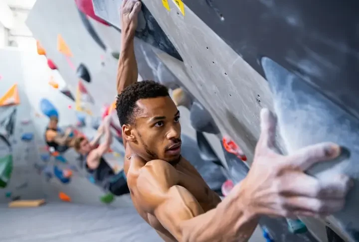 Boulderer executing a powerful move on an indoor wall, showcasing bouldering power, strong finger grip, and a solid lock-off, for a guide on building these strengths.