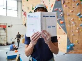 Climber with a notebook planning their session in front of a large indoor climbing wall, illustrating an effective indoor climb plan.