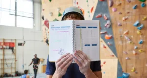 Max Your Wall Training: Effective Indoor Climb Plan Climber with a notebook planning their session in front of a large indoor climbing wall, illustrating an effective indoor climb plan.