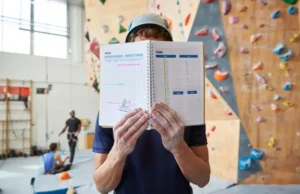 Max Your Wall Training: Effective Indoor Climb Plan Climber with a notebook planning their session in front of a large indoor climbing wall, illustrating an effective indoor climb plan.