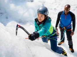 Beginner ice climber making a foundational ice axe swing on an ice wall, guided by an instructor, showcasing essential gear and moves for an ice climbing kickstart.