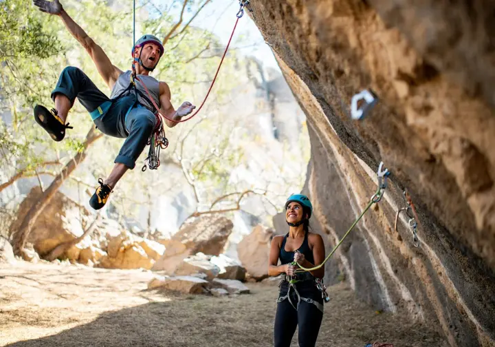 Lead climber taking a controlled fall onto a quickdraw, with an attentive belayer providing a dynamic catch, illustrating mitigation of leader fall risks.