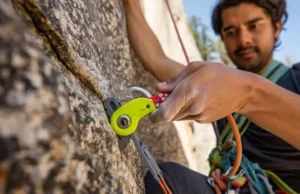Mastering Trad’s Art: Intro to Placing Protection Close-up of a climber's hands skillfully placing a camming device into a granite crack, illustrating the art and introduction to placing trad climbing protection.