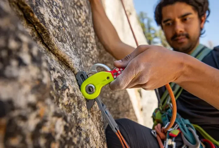 Close-up of a climber's hands skillfully placing a camming device into a granite crack, illustrating the art and introduction to placing trad climbing protection.