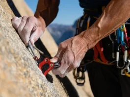 Experienced trad climber's hands expertly placing a cam in a granite crack, with nuts and slings visible on harness, mastering next-level gear placements.