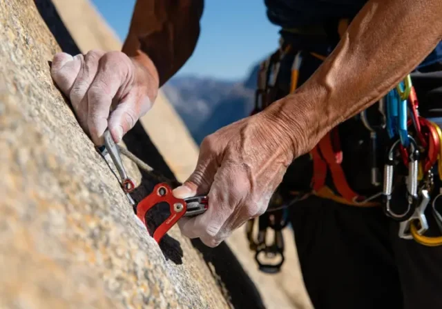 Experienced trad climber's hands expertly placing a cam in a granite crack, with nuts and slings visible on harness, mastering next-level gear placements.