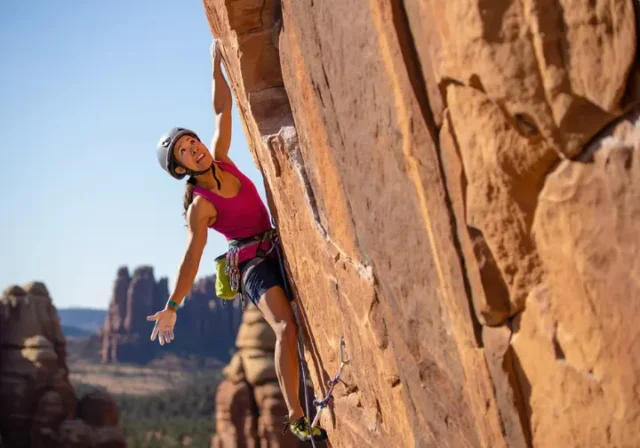 Climber on a striking sport route, with glimpses of diverse North American crags (sandstone, limestone, granite) in the background, representing top sport climbing destinations you can't miss.