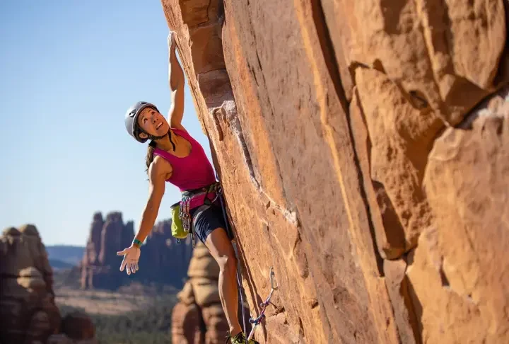 Climber on a striking sport route, with glimpses of diverse North American crags (sandstone, limestone, granite) in the background, representing top sport climbing destinations you can't miss.