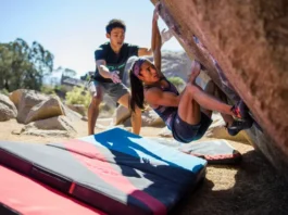 Boulderer having a fall safely guided by an attentive spotter onto well-placed crash pads at an outdoor boulder, illustrating mastering spotting and crash pad usage for safer bouldering.