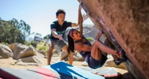 Safer Bouldering: Master Spotting & Crash Pads Boulderer having a fall safely guided by an attentive spotter onto well-placed crash pads at an outdoor boulder, illustrating mastering spotting and crash pad usage for safer bouldering.