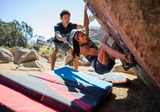 Boulderer having a fall safely guided by an attentive spotter onto well-placed crash pads at an outdoor boulder, illustrating mastering spotting and crash pad usage for safer bouldering.
