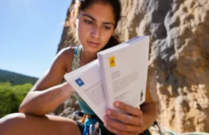 Sport Climbing Grades: YDS vs French vs UIAA Explained Climber studying a guidebook at an outdoor crag, comparing YDS, French, and UIAA sport climbing grades to understand different global systems.