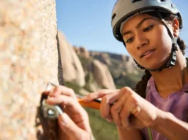 Trad climber carefully cleaning gear or brushing a hold on a pristine granite cliff, demonstrating trad climbing ethics, Leave No Trace principles, and a climber's duty for crag care.