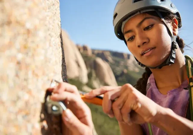 Trad climber carefully cleaning gear or brushing a hold on a pristine granite cliff, demonstrating trad climbing ethics, Leave No Trace principles, and a climber's duty for crag care.
