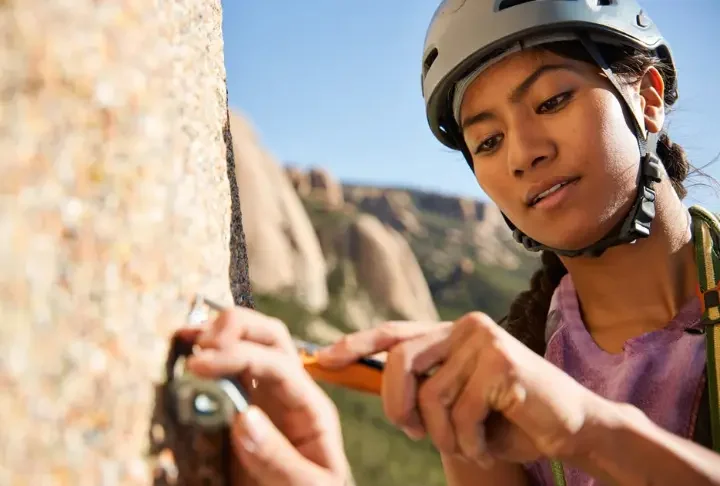 Trad climber carefully cleaning gear or brushing a hold on a pristine granite cliff, demonstrating trad climbing ethics, Leave No Trace principles, and a climber's duty for crag care.
