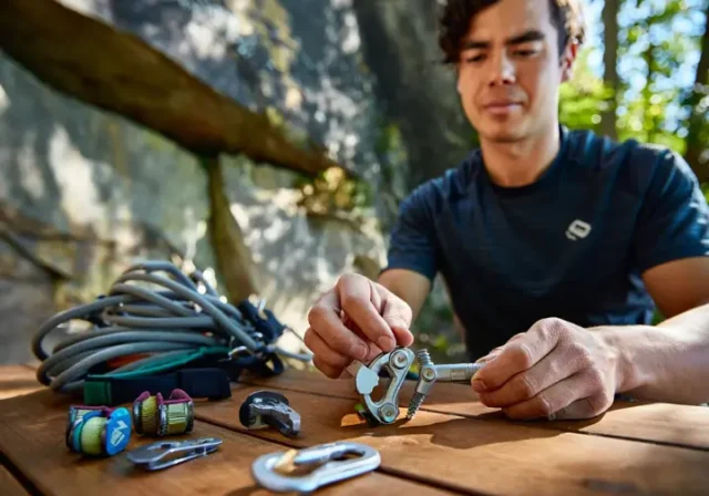 Climber organizing essential trad rack components (nuts, cams, alpine draws, nut tool) at a granite crag, prioritizing gear for building their first trad rack.