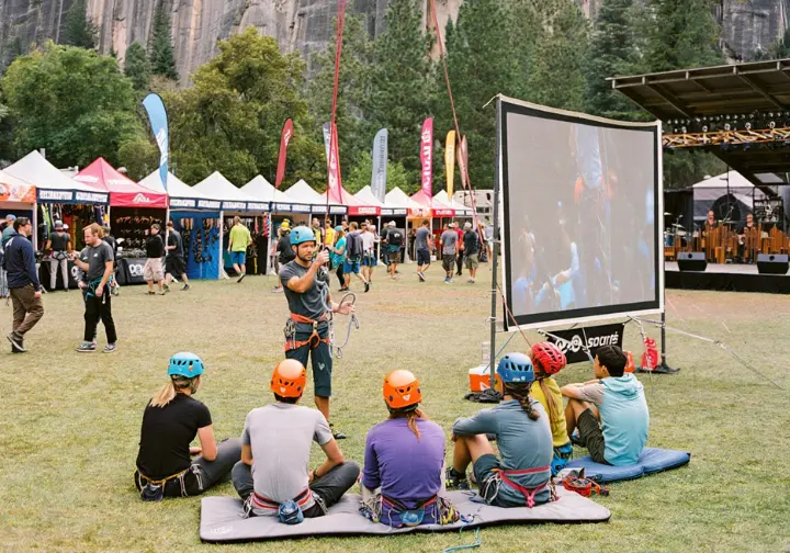 A climbing festival scene showing a skills clinic, vendor village with gear demos, and a film screen, illustrating the core components that make a "world's best" festival.