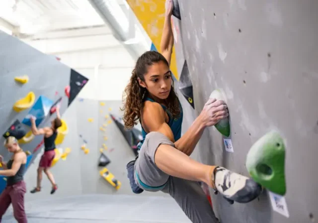 Climber making a skillful move on an intermediate indoor climbing route, progressing from beginner to intermediate indoor climbing skills with improved technique and confidence.