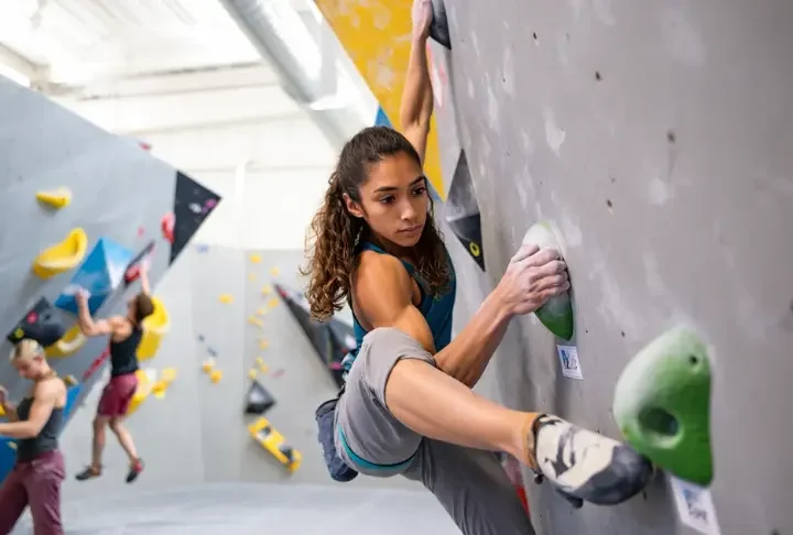 Climber making a skillful move on an intermediate indoor climbing route, progressing from beginner to intermediate indoor climbing skills with improved technique and confidence.