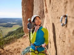 Unlock Success: Read Sport Routes Onsight, Redpoint Climber intently reading a sport climbing route from the ground, planning for onsight or redpoint success, with her belayer in the background at an outdoor crag.