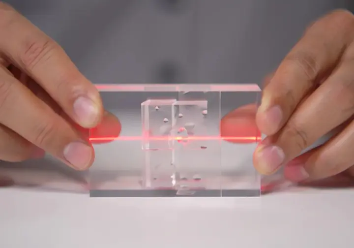 Hands holding a clear block with transparent Swiss cheese slices, a red laser showing how aligned holes lead to accident trajectory, explaining the model.