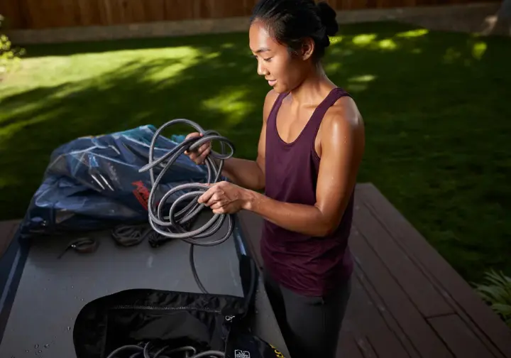 A climber carefully handling her clean climbing rope, with a rope bag and tarp nearby, demonstrating best practices for climbing rope care and maintenance.