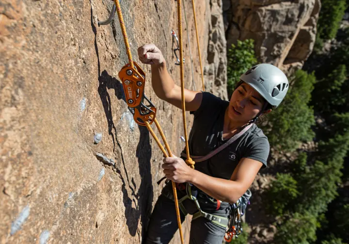 A female climber performing a top-managed lower of her partner using a guide-mode belay device, a core simple rescue technique for assisting a partner.