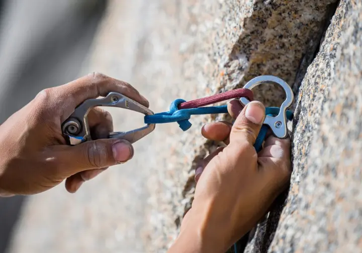 Climber's hands deconstructing a trad anchor by highlighting a core SERENE/ERNEST principle, like a solid cam placement or equalization, for building bombproof anchors.