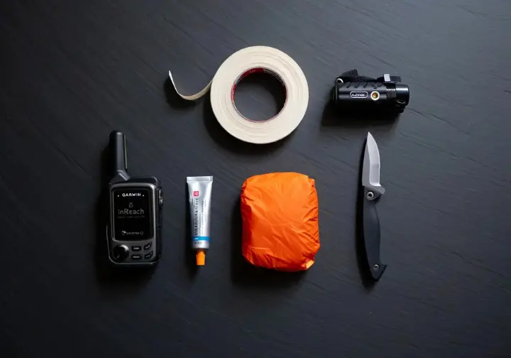 A flat lay of essential safety gear beyond the basics, including a satellite messenger, knife, and headlamp, showing what else climbers should carry.