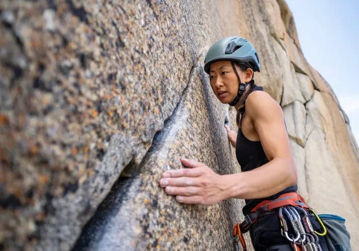 Experienced trad climber intently reading a complex granite rock face, assessing cracks and rock quality, demonstrating foundational pillars of advanced gear placement.
