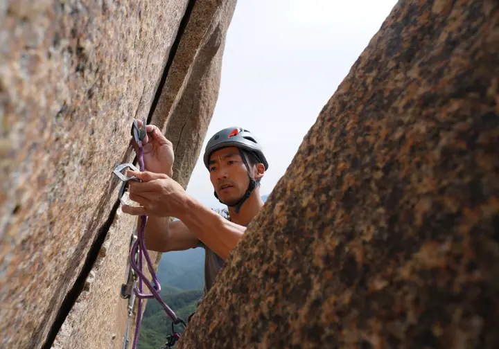 Trad climber placing removable protection on a pristine natural rock face, embodying the self-reliant and adventurous heart of traditional climbing ethics and clean climbing.