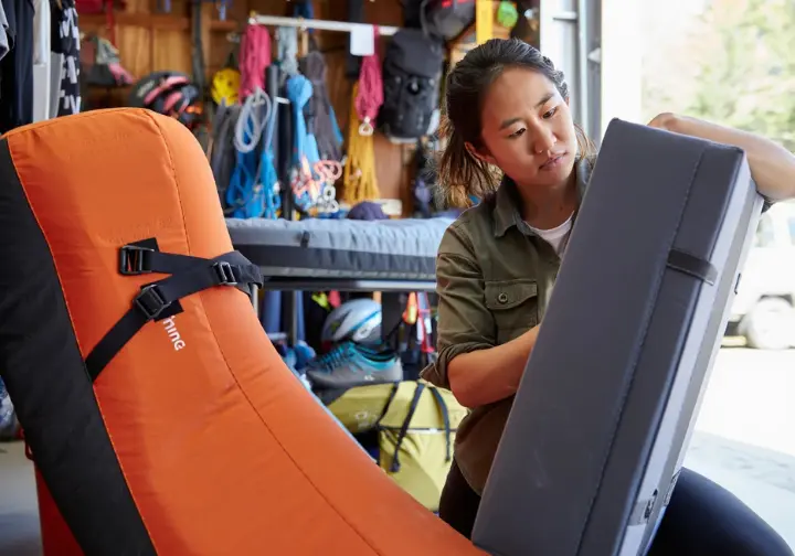 Female climber in a gear shop comparing hinge and taco style bouldering crash pads, illustrating how to choose the right one from a comprehensive guide.