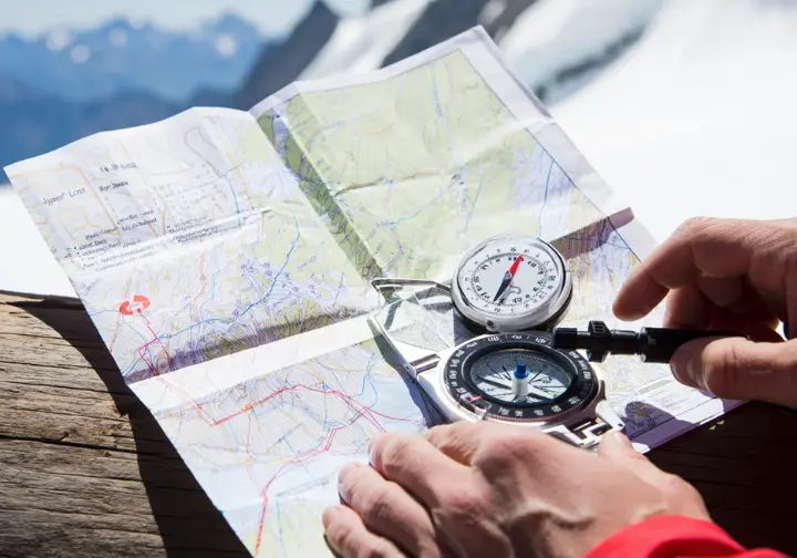 Flat lay of core alpine navigation tools: a topographic map, a baseplate compass, and an altimeter, with gloved hands interacting, illustrating mastery of these essentials.