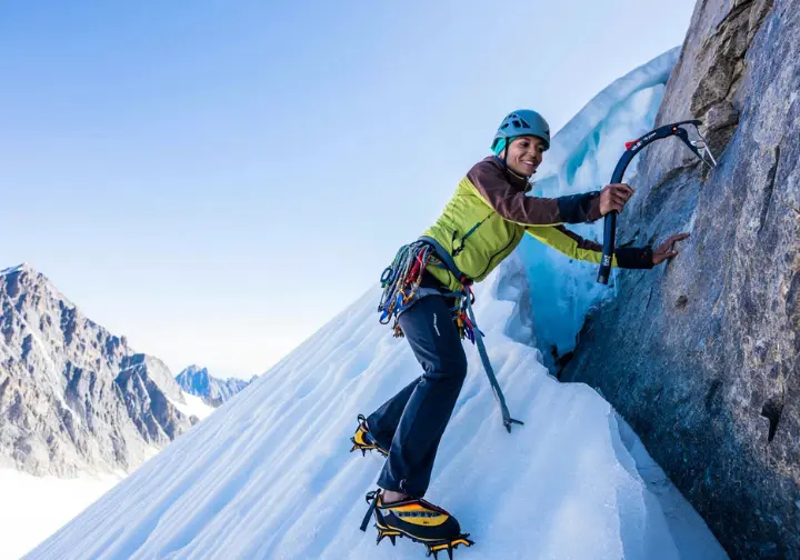 Alpinist skillfully transitioning between snow, rock, and ice on a varied alpine route, demonstrating mastery of movement and technical skills with crampons and ice axe.