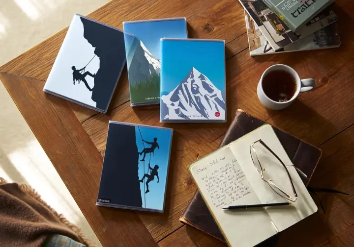A flat lay of stylized climbing film posters, a climber's journal, and coffee, representing a curated selection of must-watch films and documentaries.